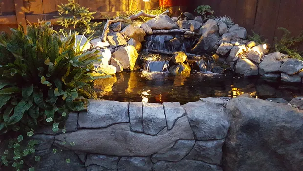Night-lit pond waterfall beside a carved salmon wall