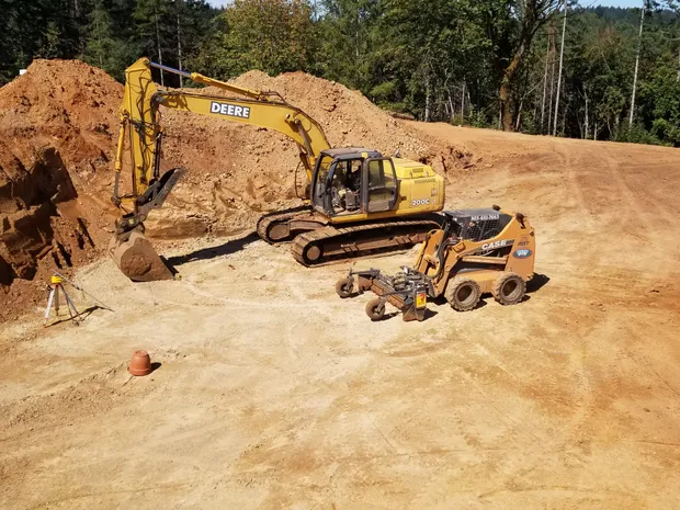 Excavator and skid steer grading a site together