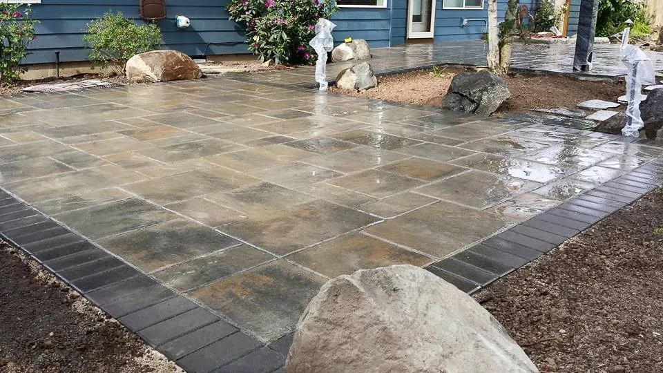 Freshly laid paver patio with boulder accents, glistening after rain