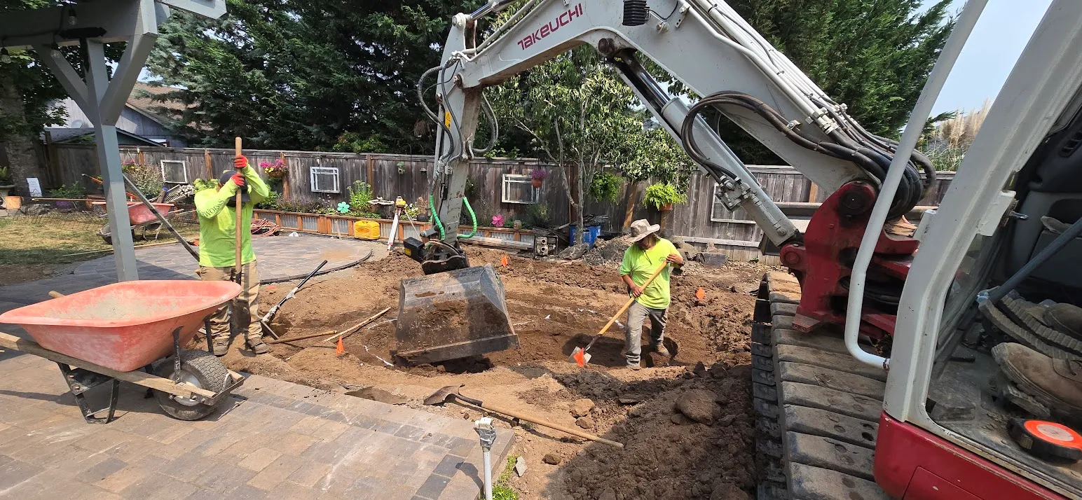Earthworks crew and mini excavator digging the pond basin in a backyard