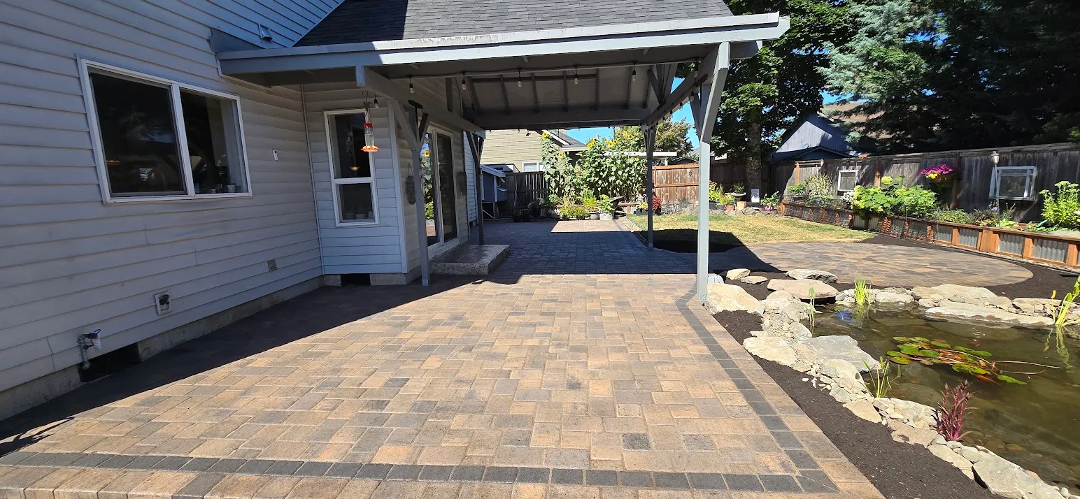 New paver patio with charcoal border banding under the same covered porch, running out to the backyard pond