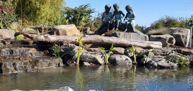 Pond waterfall with a carved statue resting on a log