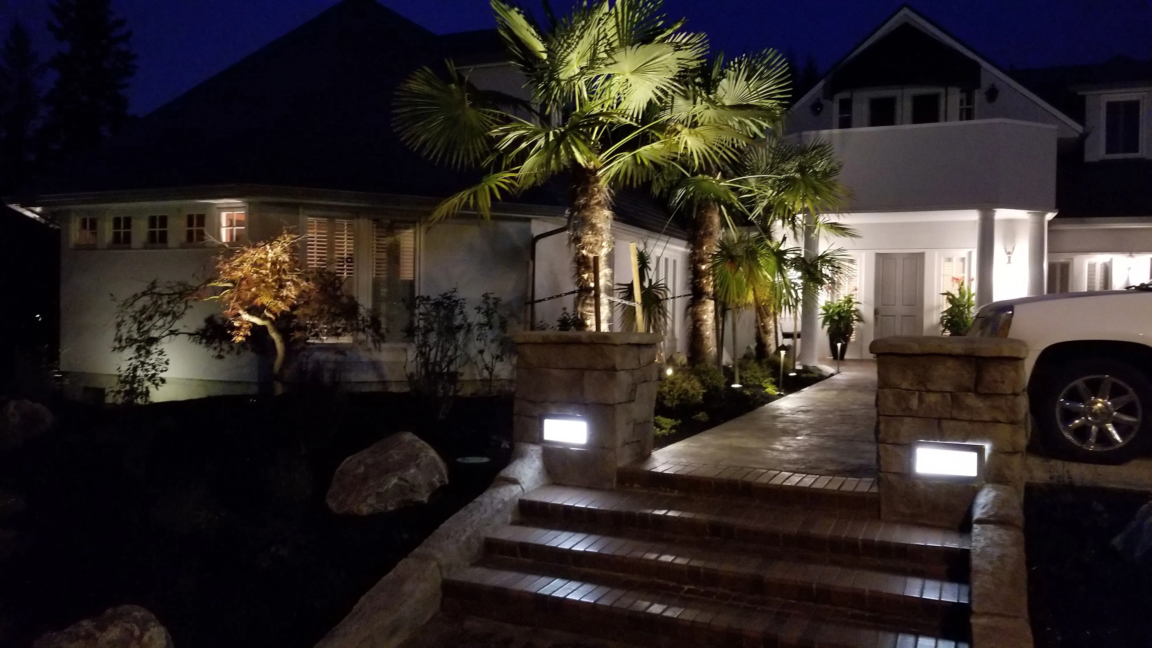 Front entry with palms, colored concrete steps, and pillars glowing under night lighting